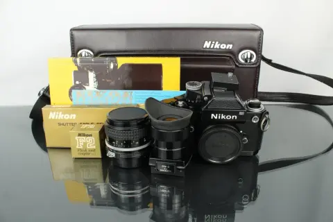 En svart Nikon F2 kamera med objektiv, blixtkopplare och originalförpackningar.