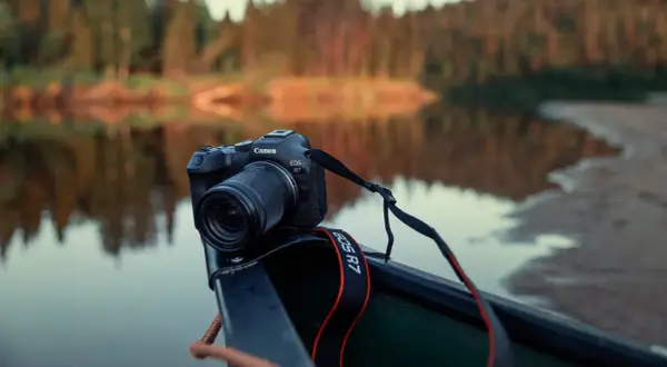 Canon EOS R7 redo i en kanot vid en spegelblank sjö med skog i bakgrunden.