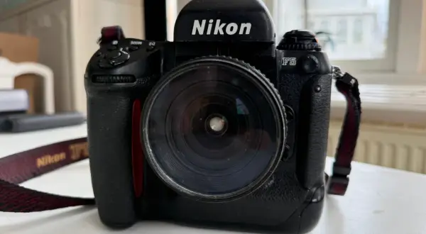 En svart Nikon F5 systemkamera med ett stort objektiv. Kameraremmen med texten "Nikon" syns.