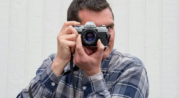 Man med rutig skjorta håller upp en Minolta-kamera för att fota analogt.