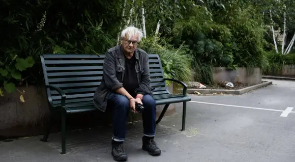 Anders Petersen sitter på en parkbänk, omgiven av grönska.