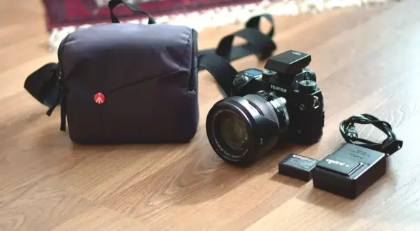 En Fujifilm XH1-kamera med objektiv, batteri, laddare och väska ligger på ett trägolv.