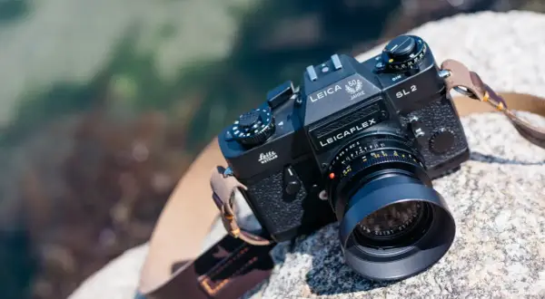 En svart Leicaflex SL2-kamera med ett objektiv och en läderrem ligger på en sten vid vattnet.