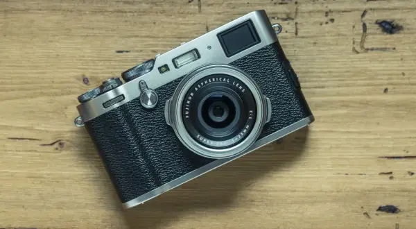 En Fujifilm X100T-kamera ligger på en träyta. Dess retrodesign och fasta objektiv gör den till en favorit för gatufotografering.
