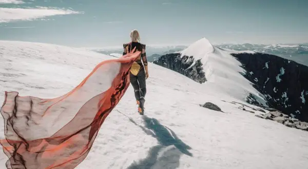 En kvinna med röd sjal vandrar på ett snötäckt berg. Emma Svensson fotograf.