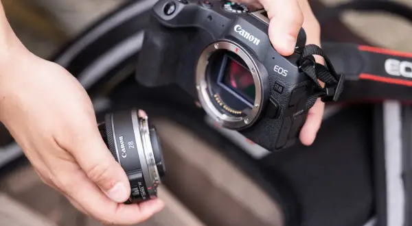 Händer byter objektiv på en Canon EOS R8. Vad betyder RF? Det är objektivfattningen, som på denna kamera är RF-fattning.