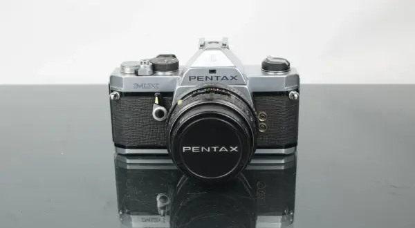 En klassisk Pentax MX-kamera med objektivlock.