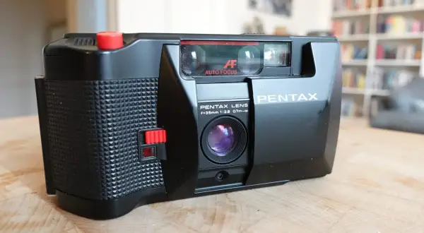 En svart Pentax PC35AF-kamera med autofokus och en 35mm lins ligger på ett träbord.