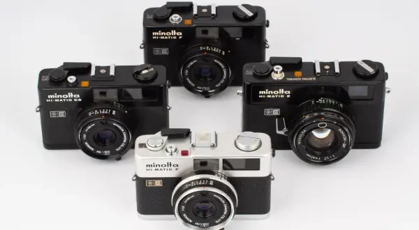 Fyra Minolta Hi-Matic kameror, varav en silverfärgad Minolta Hi-Matic F i förgrunden, omgivna av svarta modeller.