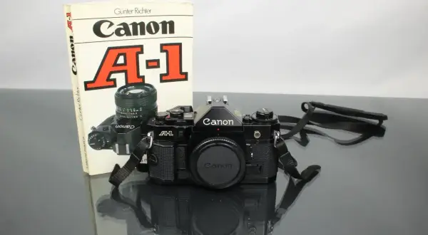 Svart Canon A-1 systemkamera med objektiv och en bok om kameran. En klassiker för den som vill lära sig mer om analog fotografering.