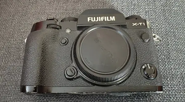 En svart Fujifilm X-T1 kamera ligger på en grå bakgrund.