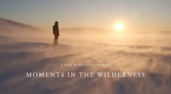En ensam person står i snöstormen, en film av Magnus Lindbom. Solen går ner över ett öde landskap.