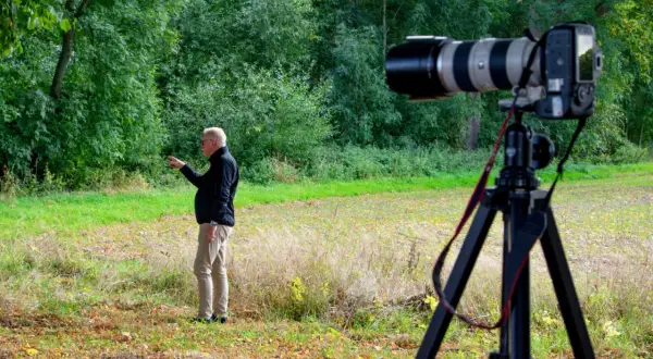 Man pekar i skogen. En kamera på stativ är redo för bildanalys.