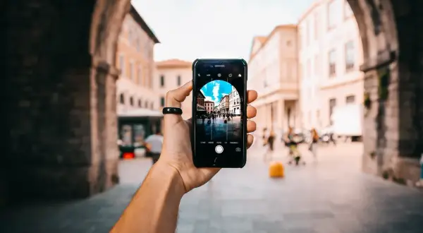 En hand håller upp en iPhone för att ta bra bilder med iPhone av en livlig stadsgata sedd genom en stenbåge.