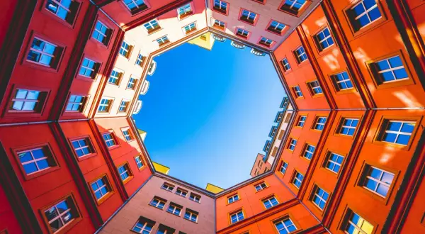 Fasaderna på ett färgglatt hus bildar en cirkel runt en klarblå himmel. Fönstren är många och speglar ljuset. En vacker vy att skapa bild av.
