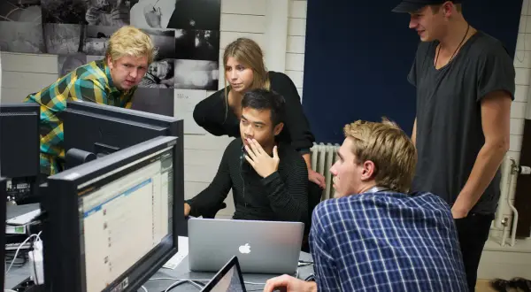 Studenter på **Nordens Fotoskola** diskuterar projekt framför datorskärmar.