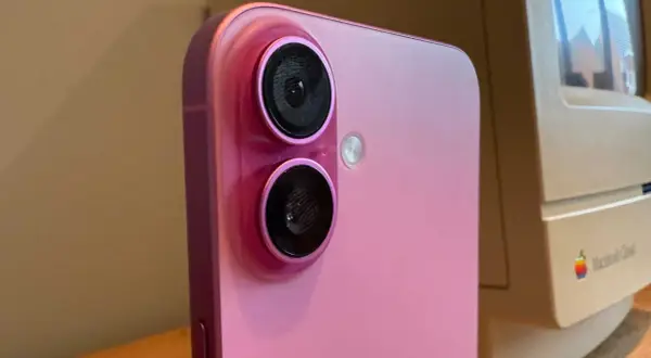 Rosa iPhone med dubbla linser på kameran, bredvid en gammal Macintosh-dator.