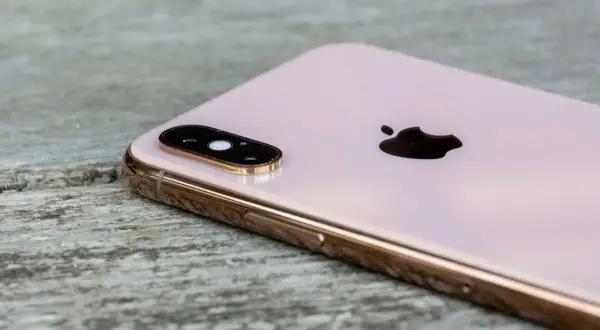 En rosa iPhone XS med dubbla linser på kameran, placerad på en träyta.