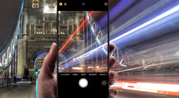 En hand håller en iPhone som fångar ljusspår från bilar vid Tower Bridge. En lång slutartid på iPhone ger en dramatisk effekt.