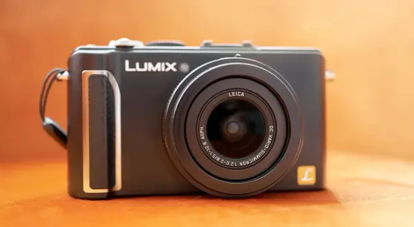 Svart kompaktkamera, en Lumix LX3 med Leica-objektiv, ligger på en orange yta.