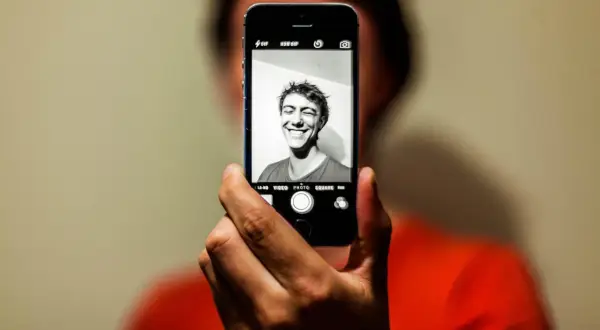 En person tar en selfie med en iPhone. Personen ler brett mot kameran.