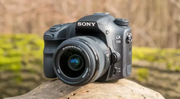 Sony a68 systemkamera med objektiv, placerad på en trädstam utomhus.