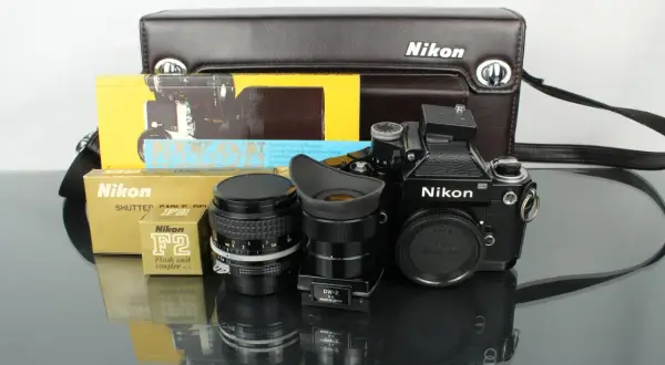 En svart Nikon F2 kamera med objektiv, blixtkopplare och originalförpackningar.