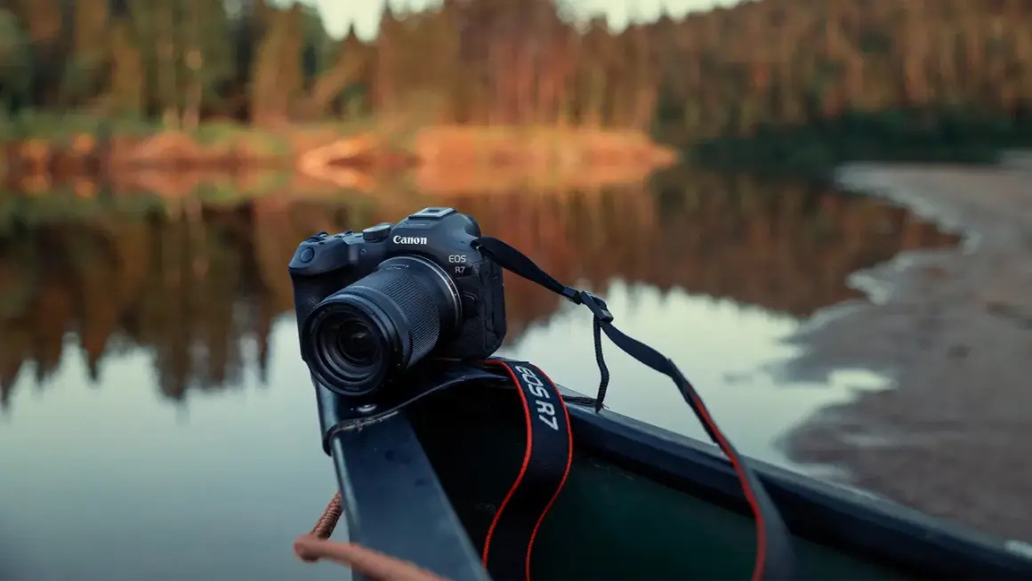 Canon EOS R7 redo i en kanot vid en spegelblank sjö med skog i bakgrunden.