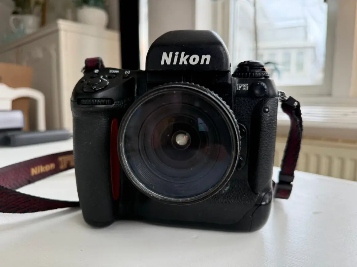 En svart Nikon F5 systemkamera med ett stort objektiv. Kameraremmen med texten "Nikon" syns.