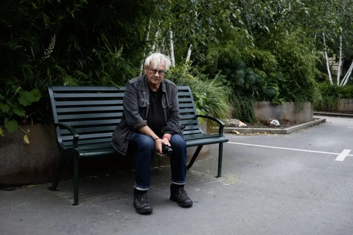 Anders Petersen sitter på en parkbänk, omgiven av grönska.