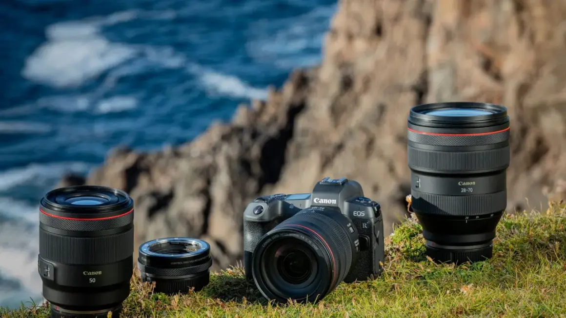 Canon R-serie kamerahus och objektiv, inklusive 50mm och 28-70mm, placerade på en gräsbevuxen klippa vid havet.