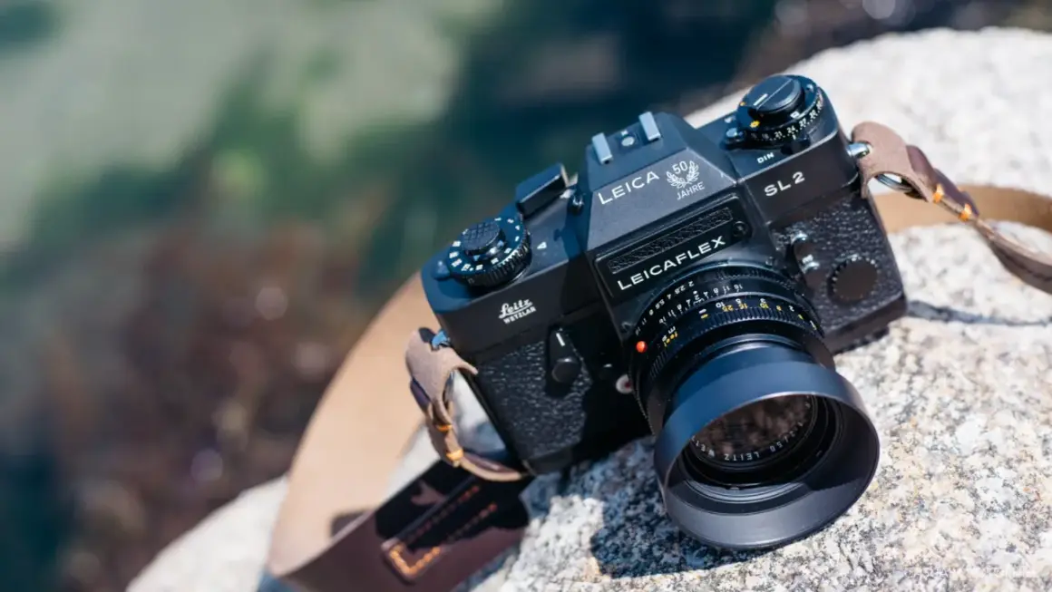 En svart Leicaflex SL2-kamera med ett objektiv och en läderrem ligger på en sten vid vattnet.