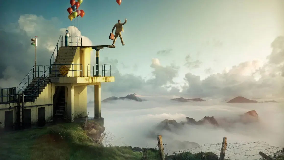 En man med portfölj och ballonger står på en dykplattform över moln. Erik Johansson fotograf.