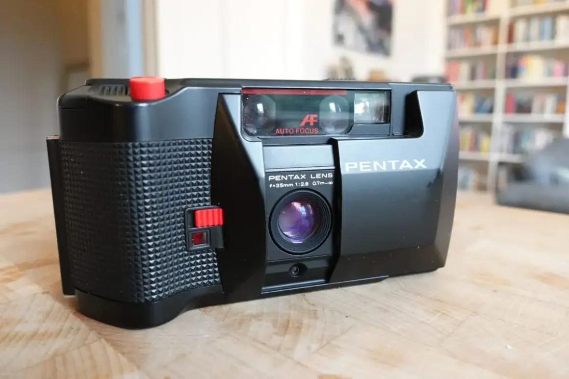 En svart Pentax PC35AF-kamera med autofokus och en 35mm lins ligger på ett träbord.