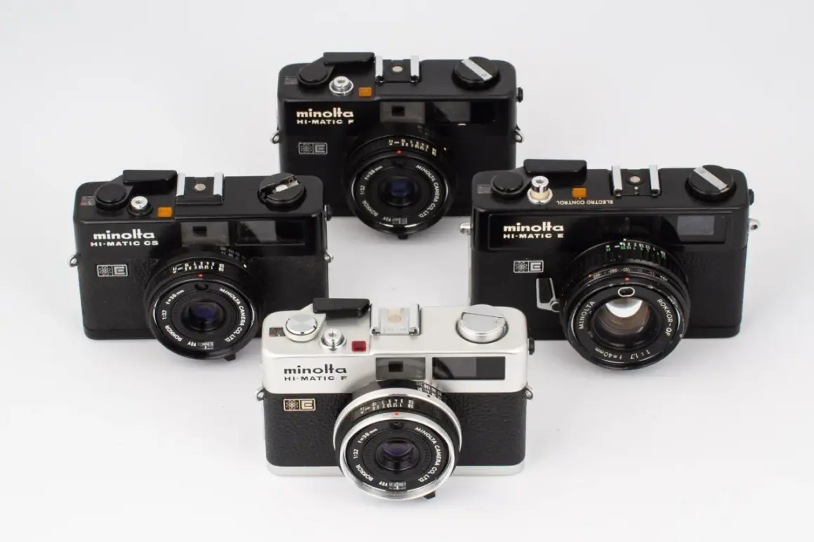 Fyra Minolta Hi-Matic kameror, varav en silverfärgad Minolta Hi-Matic F i förgrunden, omgivna av svarta modeller.
