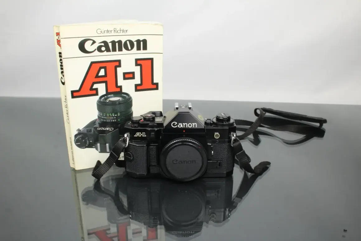 Svart Canon A-1 systemkamera med objektiv och en bok om kameran. En klassiker för den som vill lära sig mer om analog fotografering.