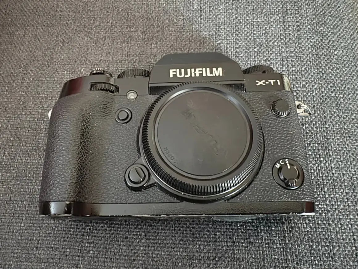 En svart Fujifilm X-T1 kamera ligger på en grå bakgrund.