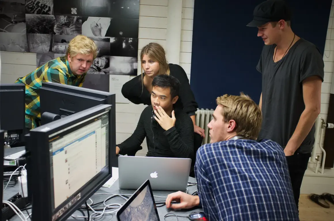 Studenter på **Nordens Fotoskola** diskuterar projekt framför datorskärmar.