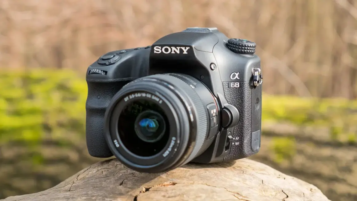 Sony a68 systemkamera med objektiv, placerad på en trädstam utomhus.