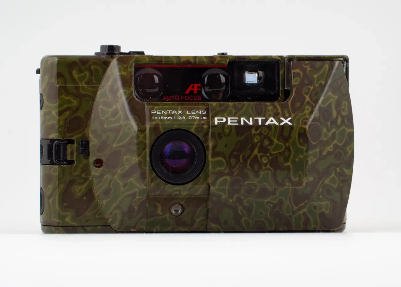 En kamouflerad Pentax PC35AF-kamera med autofokus. Perfekt f&ouml;r att sm&auml;lta in i naturen och f&aring;nga &ouml;gonblicken.