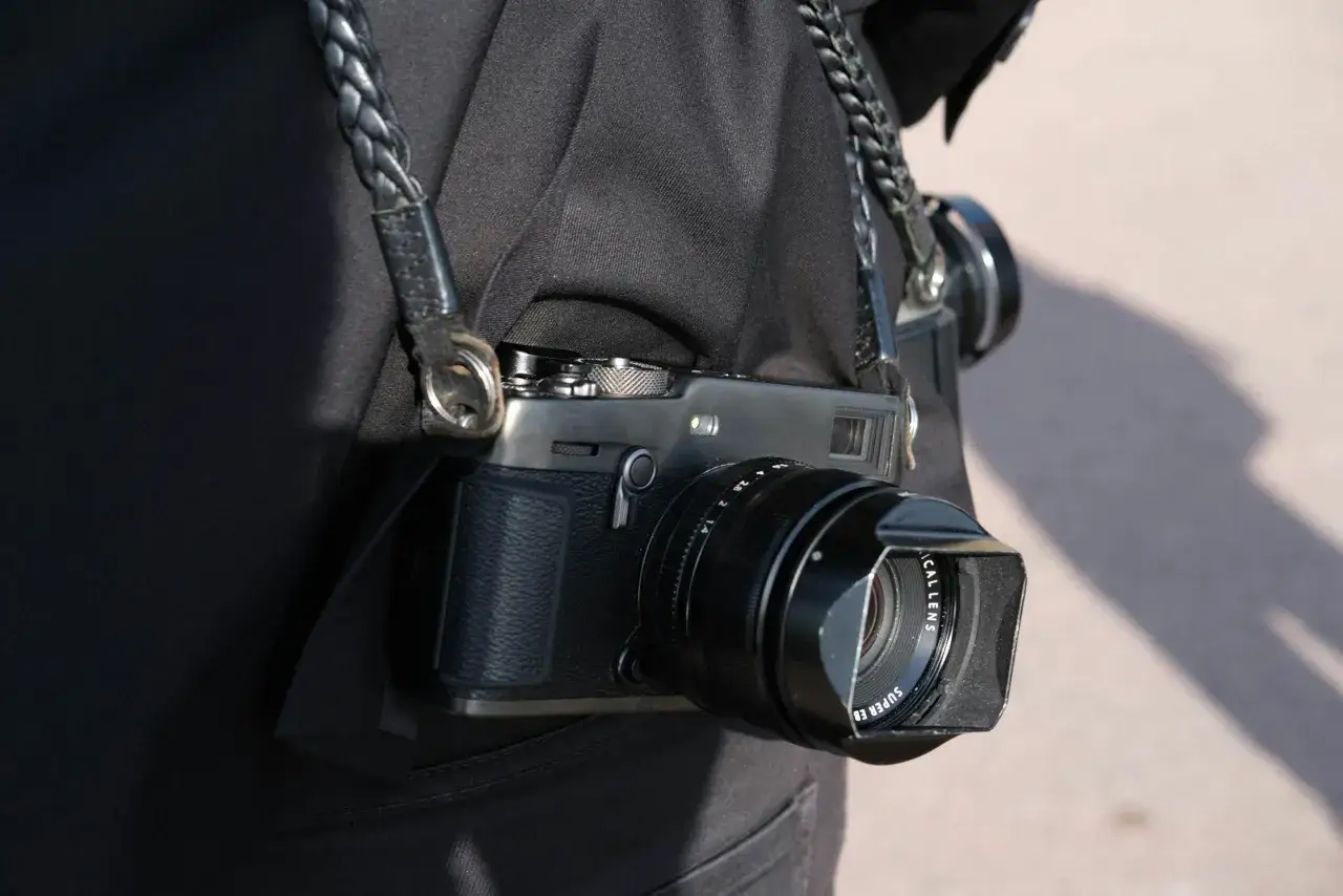 En person bär en svart jacka med en flätad läderrem som håller en Fuji Xpro 3-kamera.