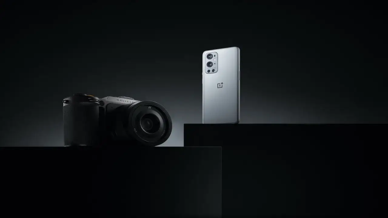 En stilren bild som visar en OnePlus-telefon bredvid en Hasselblad-kamera, båda i en mörk och dramatisk miljö.