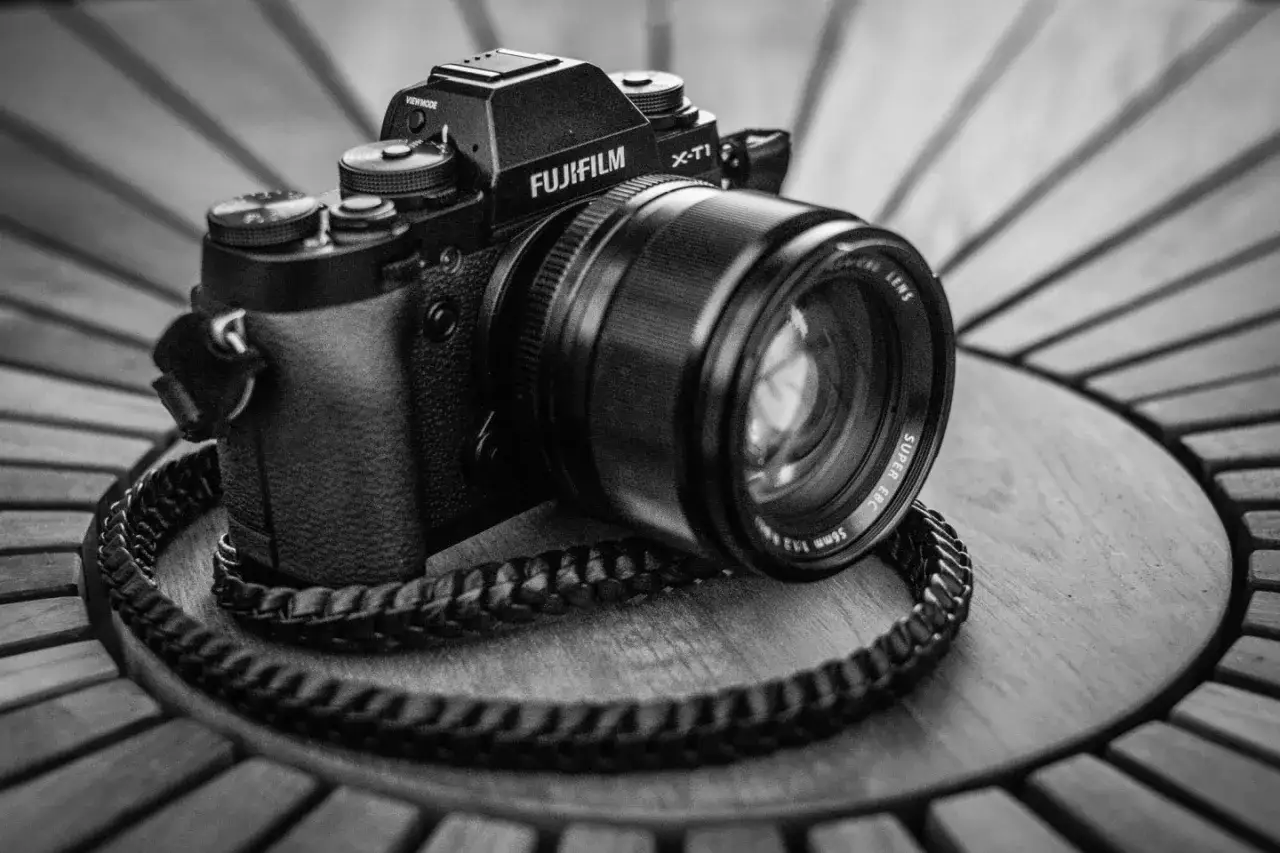 En svartvit bild p&aring; en Fujifilm X-T1 kamera med en l&auml;derrem, placerad p&aring; ett tr&auml;bord.