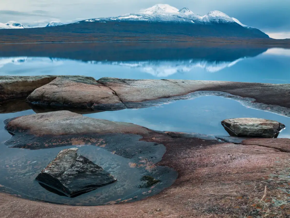 Steniga str&auml;nder med vattenp&ouml;lar reflekterar sn&ouml;kl&auml;dda berg. En vy som f&aring;ngats av Serkan Gunes.