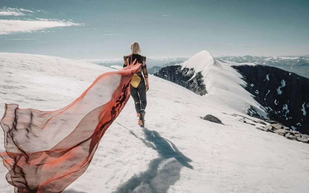En kvinna med röd sjal vandrar på snöklädda berg. Emma Svensson fotograf fångar den dramatiska vyn.