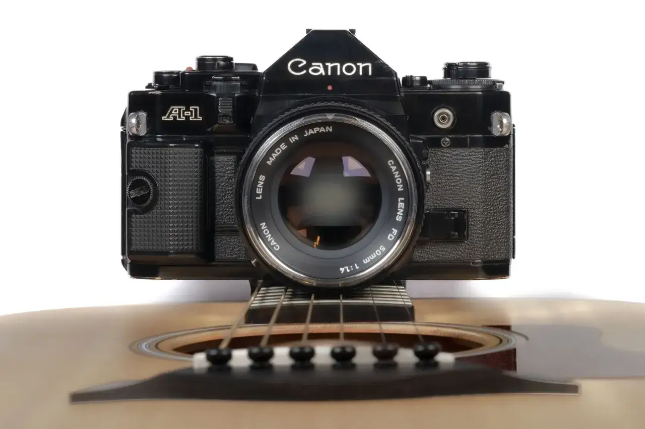 En svart Canon A-1 kamera vilar på en akustisk gitarr.