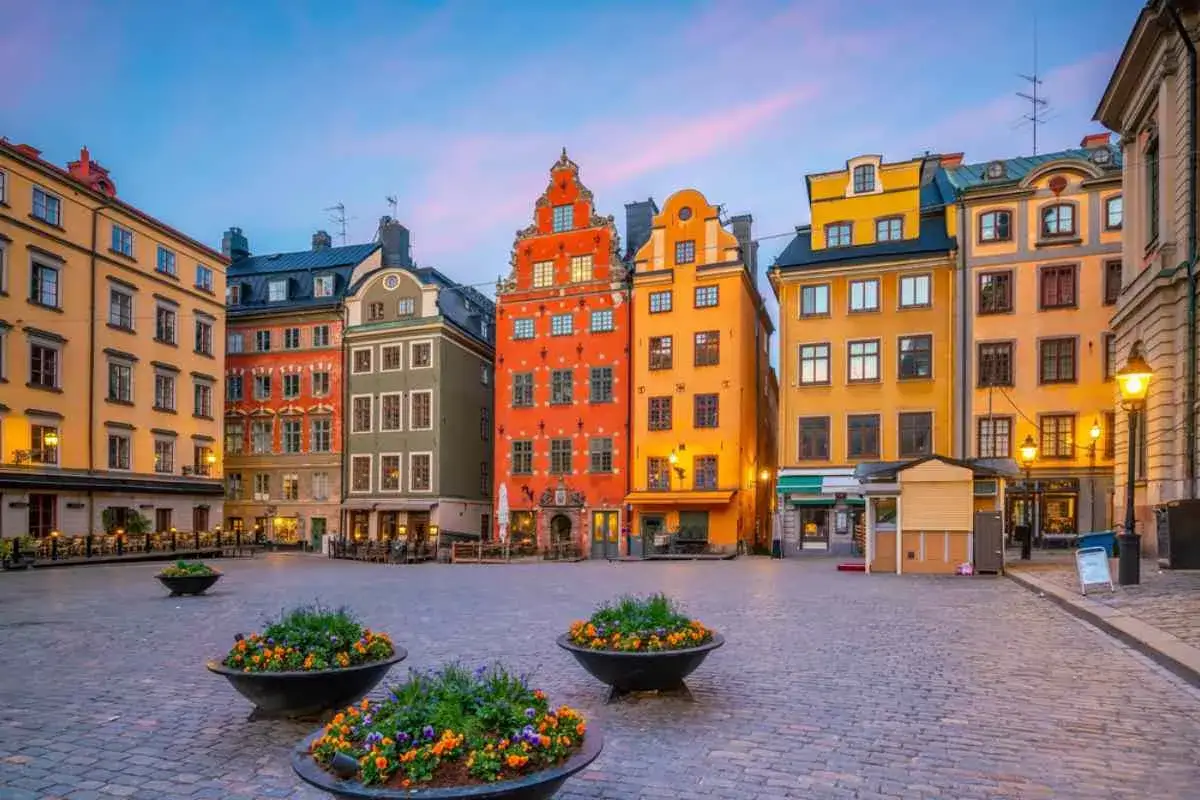 Färgglada hus på ett torg i Stockholm, som hämtade ur gamla stockholmsbilder. Blommor i krukor på kullerstensbelagd mark.