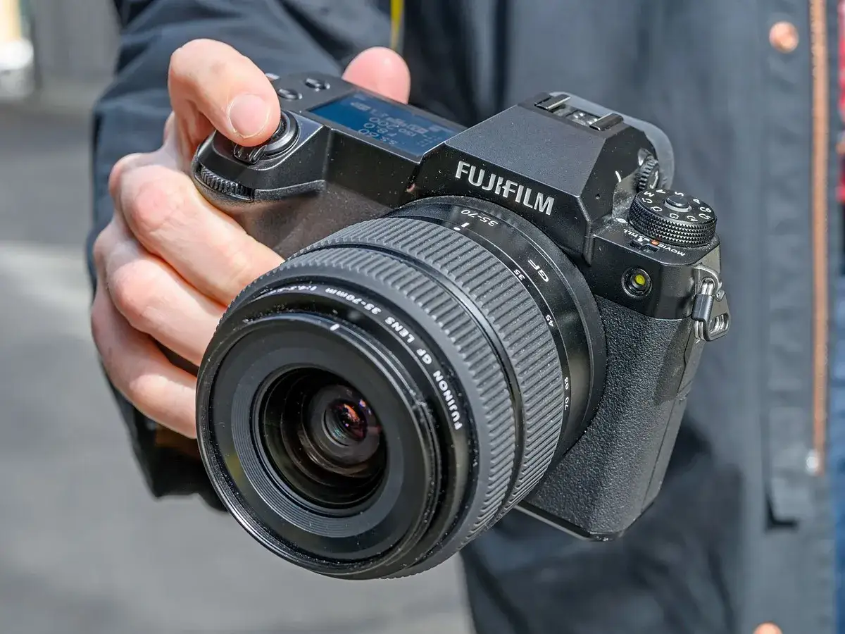 En hand håller en Fujifilm GFX 50S II med ett GF 35-70mm objektiv.