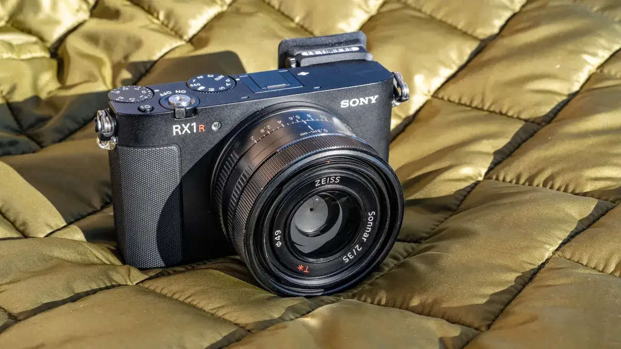 En svart Sony RX1R-kamera med ett Zeiss Sonnar 2/35-objektiv ligger på ett olivgrönt, quiltat tyg.