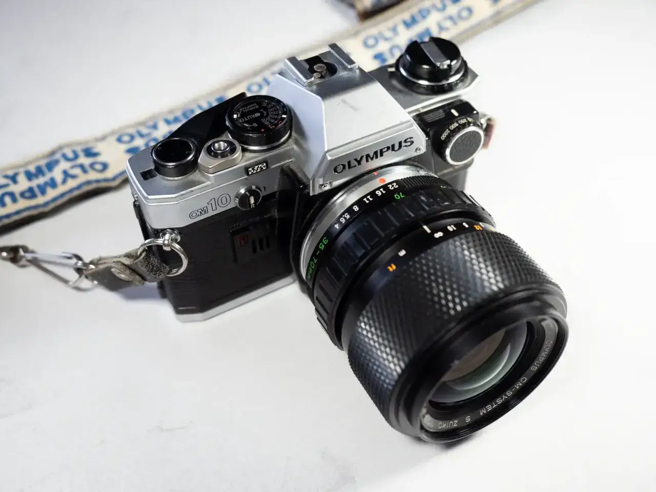 En klassisk Olympus OM-10 systemkamera med objektiv och en Olympus-rem. Perfekt för att fånga minnen.